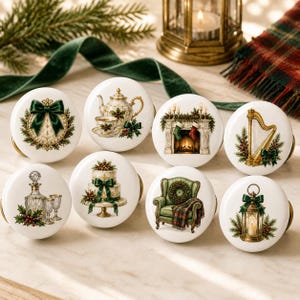 Könnte beinhalten: Ein Set aus acht runden, weißen Keramik-Möbelknöpfen mit weihnachtlichen Motiven, darunter eine grüne Schleife, eine Teekanne, ein Kamin mit Strümpfen, eine Harfe, eine Kristallkaraffe, eine Torte, ein grüner Sessel und eine Laterne.