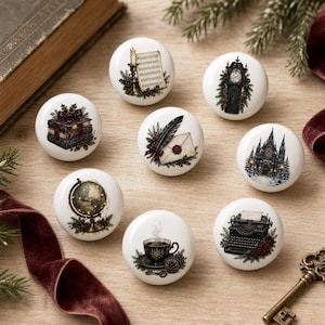 May include: A set of eight round white ceramic cabinet knobs, each featuring a unique vintage-style illustration including a candle with sheet music, a grandfather clock, stacked books, a letter with a quill, a cathedral, a globe, a coffee cup, and a typewriter.