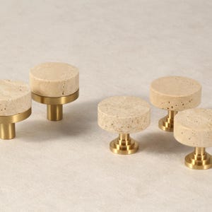 Peut inclure: Ensemble de cinq boutons de meuble. Chaque bouton est composé d'un dessus rond en pierre beige clair et d'une base en laiton. Ces boutons sont conçus pour les meubles et la décoration intérieure.