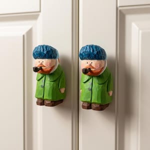 Puede incluir: Dos pomos de armario de madera tallados a mano con forma de figuras que llevan gorros azules, abrigos verdes y zapatos marrones. Cada figura tiene una barba de color marrón rojizo y sostiene una pequeña pipa negra en la boca.
