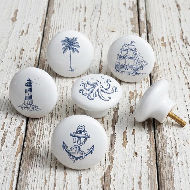 以下が含まれることがあります： 白のセラミック製キャビネットノブのコレクションで、航海をテーマにしたデザインです。各ノブには、灯台、帆船、ヤシの木、錨、タコなど、さまざまな青色のイラストが描かれています。1つのノブはネジ付きで表示されています。
