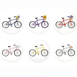 May include: Six round decorative buttons featuring bicycle illustrations. Each button showcases a different colored bicycle, including purple, red, pink, yellow, gray, and blue. Some bicycles have baskets with flowers or sunflowers.