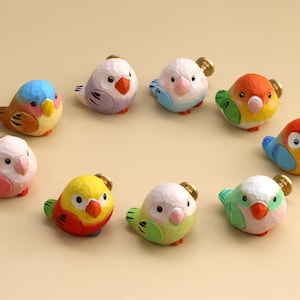 May include: A collection of nine small, hand-carved wooden bird-shaped drawer knobs. Each knob features a unique color combination, including shades of blue, orange, yellow, pink, and green, with a metallic screw attachment on the back of each.