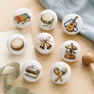May include: A set of eight round white ceramic knobs, each featuring a distinct illustration: a colourful xylophone, a tambourine with a green ribbon, a wooden guitar, a drum, two brass bells with a bow, a carousel, a harmonica, and two maracas.