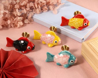 May include: Four ceramic fish drawer pulls in various colors. The fish are in shades of red, yellow, pink, and blue. The fish have gold metal hardware.