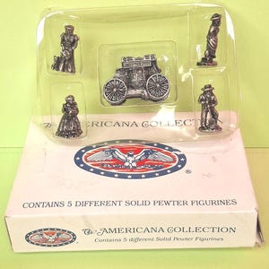 May include: A set of five solid pewter figurines in a clear plastic tray, presented on a white box. The figurines depict historical figures and a stagecoach. The box reads "AMERICANA COLLECTION" and "CONTAINS 5 DIFFERENT SOLID PEWTER FIGURINES."