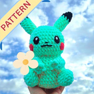 Puede incluir: Un peluche de Pikachu de ganchillo turquesa hecho a mano con orejas con puntas negras, mejillas rojas y boca y ojos negros. El peluche sostiene una flor blanca con un centro amarillo. La palabra "PATTERN" está en una pancarta amarilla en la esquina superior izquierda.