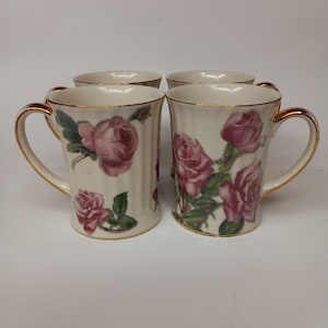 May include: Set of four white ceramic mugs with gold trim and a pink rose floral design.