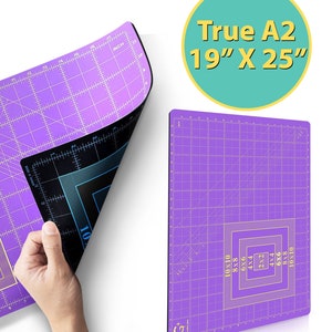 May include: A purple self-healing cutting mat with a grid pattern and gold markings. The mat is 19 inches by 25 inches and is labeled "True A2".