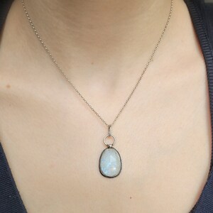 Puede incluir: Un collar de cadena de plata con un colgante con una piedra de luna grande de forma ovalada con un engaste de plata.