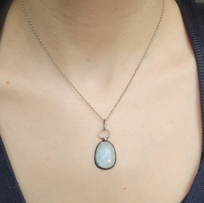 Puede incluir: Un collar de cadena de plata con un colgante con una piedra de luna grande de forma ovalada con un engaste de plata.