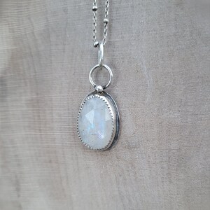 Puede incluir: Un collar de cadena de plata con un colgante de piedra lunar blanca. El colgante tiene forma ovalada y tiene un engaste de bisel de plata.