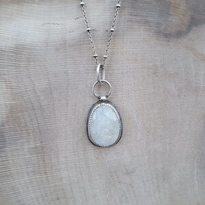 Puede incluir: Un collar de cadena de plata con un colgante ovalado blanco con un cristal transparente. El colgante est&aacute; engastado en un bisel de plata y tiene una delicada argolla de plata.