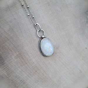 Puede incluir: Un collar de cadena de plata con un colgante de piedra lunar blanca. El colgante est&aacute; engastado en un bisel de plata y tiene un borde delicado y festoneado.