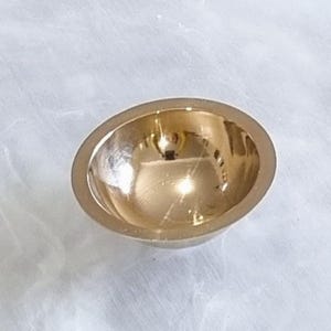 May include: A small, round, gold-colored metal bowl. The bowl is smooth and shiny, with a slight indentation in the center.