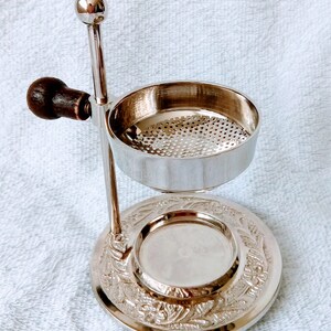May include: Silver incense burner with a decorative base and a removable top with a perforated metal insert. The burner has a wooden handle.