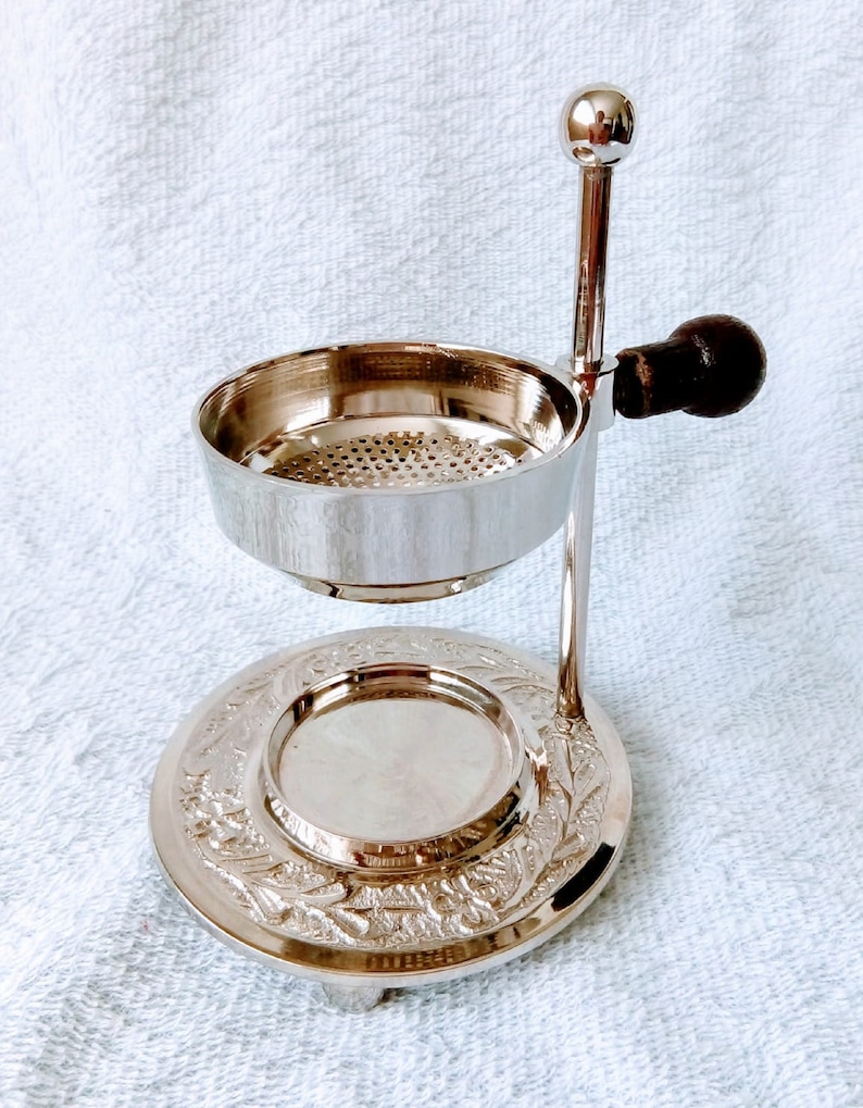 May include: Silver incense burner with a round base and a decorative design. The burner has a removable bowl with a mesh screen and a handle.