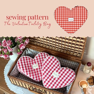 May include: Two heart-shaped toiletry bags with red and white gingham pattern inside a wicker basket. The bags have a small white label with the brand name. The text "sewing pattern The Valentine Toiletry Bag" is visible.