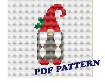 May include: A cross-stitch pattern for a red and white gnome with a green leaf on its hat. The pattern is framed in a red frame and the words "PDF PATTERN" are printed in blue below the gnome.