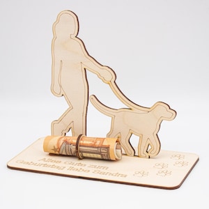 Könnte beinhalten: Holzschnitt einer Person, die einen Hund spazieren führt, mit einem eingerollten Geldschein in der Basis. Die Basis ist mit dem Text "Alles Gute zum Geburtstag liebe Sandra" beschriftet.