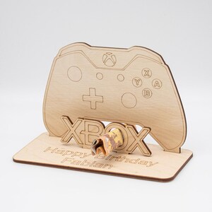Könnte beinhalten: Ein Holzständer für einen Xbox-Controller mit dem Wort "Xbox" auf der Vorderseite. Der Ständer hat einen Schlitz für eine Geschenkkarte oder Geld. Der Ständer ist mit dem Text "Happy Birthday Fabian" personalisiert.
