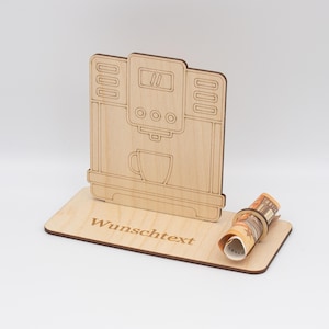 Könnte beinhalten: Ein hölzerner Kaffeemaschinen-Geldhalter mit einem Schlitz für gerollte Geldscheine. Die Basis hat den Text "Wunschtext" eingraviert.