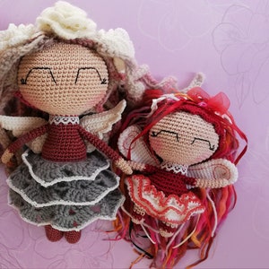 Puede incluir: Dos muñecas de crochet con alas, una con una falda gris y la otra con una falda roja, sobre un fondo rosa. Las muñecas se llaman Willa y Garnet.