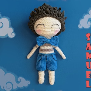May include: A crocheted doll with brown hair, wearing a blue and white striped shirt, blue shorts, and a blue bow tie. The doll is lying on a blue background with white clouds and the name "SAMUEL" written in red letters.