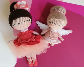 Puede incluir: Dos muñecas de crochet, una con un vestido rosa con falda de tul y una corona de flores, la otra con un vestido rosa con alas blancas.
