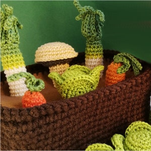 Könnte beinhalten: Ein brauner gehäkelter Topf gefüllt mit gehäkeltem Gemüse, darunter ein Pilz, Karotten und Lauch.