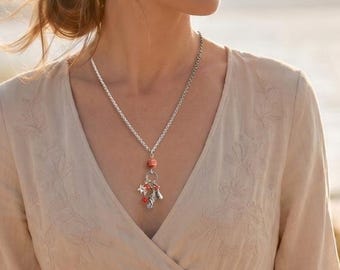 May include: A beige long-sleeved dress with a V-neckline and subtle tonal embroidery on the bodice. A silver-toned chain necklace features a central orange bead and a cluster of small silver charms hanging from the bottom of the chain.