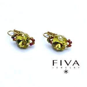 May include: Gold-plated leverback earrings featuring large, oval, olive-green crystals. Each crystal is encircled with small, iridescent beads. The earrings are set against a white backdrop, with the brand name "FIVA JEWELRY" in black.