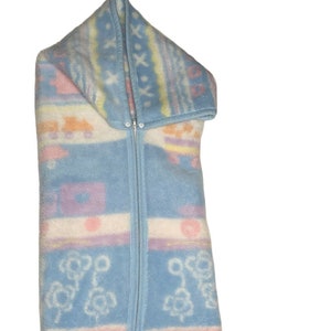 May include: A blue baby sleeping bag with a zipper down the front and a hood. The bag has a colorful pattern with flowers and geometric shapes.