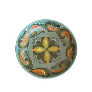 May include: A round, hand-painted decorative bowl with a teal rim and a gray interior. The bowl features a central floral design in shades of brown and yellow, surrounded by ornate, swirling patterns in orange and green.