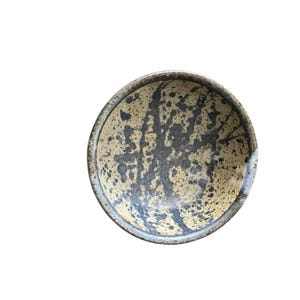 May include: A small, round ceramic bowl with a speckled brown glaze and blue and black splatter paint design.