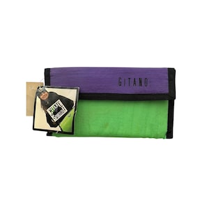 May include: A vintage wallet with a purple top, green bottom, and black trim. The word "GITANO" is printed on the purple section. A tag is attached with a photo of a person wearing a jacket with the words "GITANO Sportline".