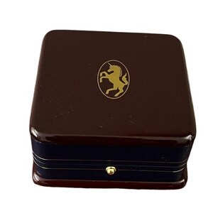 May include: A dark brown wooden box with a gold unicorn logo on the top. The box has a blue velvet lining and a gold latch.