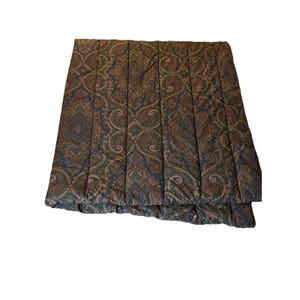 Op de afbeelding: Een rechthoekig gewatteerd dekbed met een herhalend paisley-patroon in tinten donkerbruin, bosgroen en gedempt blauw. De stof is doorgestikt met verticale banen die over de lengte van het item lopen, wat zorgt voor een textuur op het oppervlak.
