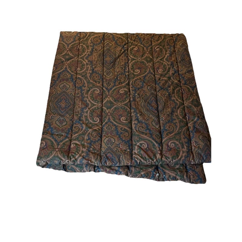 Op de afbeelding: Een rechthoekig gewatteerd dekbed met een herhalend paisley-patroon in tinten donkerbruin, bosgroen en gedempt blauw. De stof is doorgestikt met verticale banen die over de lengte van het item lopen, wat zorgt voor een textuur op het oppervlak.