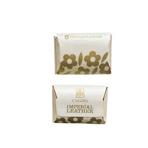 May include: Two small white soap bars with gold lettering. The top bar has a floral design and the text "Shangri-La hotel HONG KONG". The bottom bar has the text "Cussons IMPERIAL LEATHER".