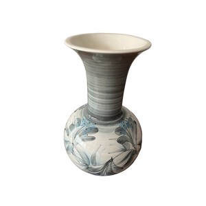 May include: A white ceramic vase with a gray and blue floral design. The vase has a round body and a flared opening.