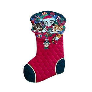 May include: A quilted Christmas stocking in red with dark green trim. The cuff features an embroidered scene of a Dalmatian puppy in a Santa hat, a tabby kitten, a calico kitten, wrapped gifts, candy canes, and a birdhouse ornament.