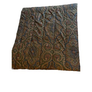 Op de afbeelding: Een rechthoekig gewatteerd dekbed met een herhalend paisley-patroon in tinten donkerblauw, bosgroen en gedempt roestoranje. De stof is doorgestikt met verticale banen die over de gehele lengte lopen, wat zorgt voor een getextureerd oppervlak.
