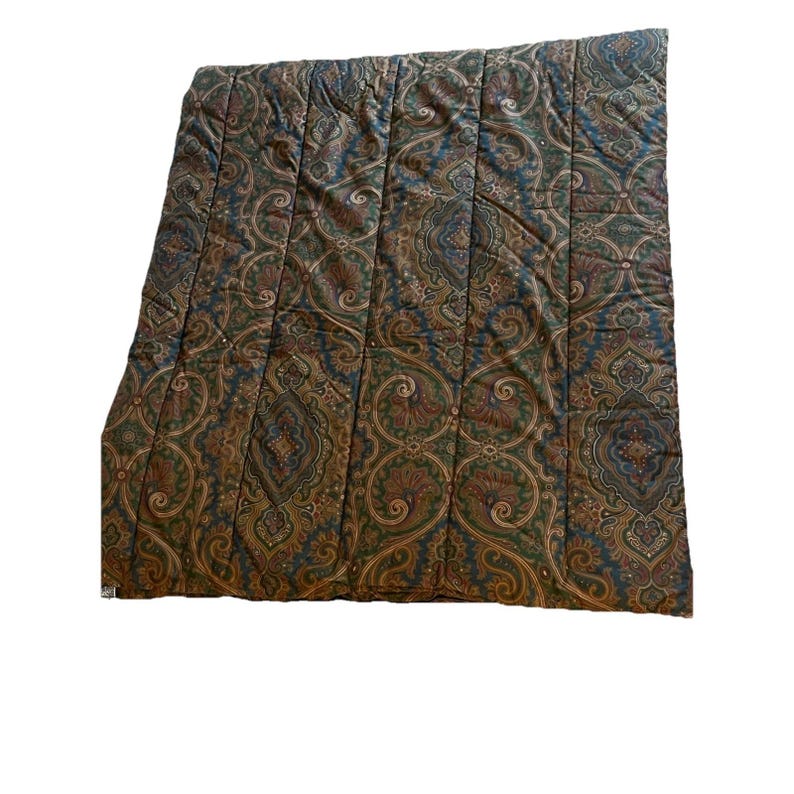 Op de afbeelding: Een rechthoekig gewatteerd dekbed met een herhalend paisley-patroon in tinten donkerblauw, bosgroen en gedempt roestoranje. De stof is doorgestikt met verticale banen die over de gehele lengte lopen, wat zorgt voor een getextureerd oppervlak.
