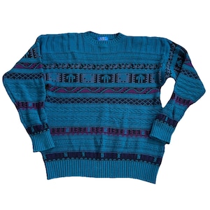 May include: Teal-colored sweater with a crew neck and long sleeves. The sweater features a geometric pattern in purple, black, and gray. The cuffs and hem are ribbed. The label reads "CUBI".