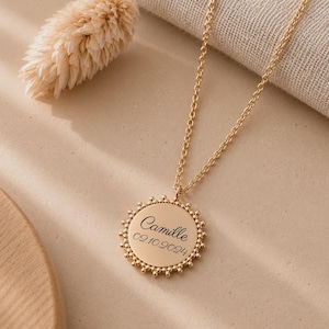 Peut inclure: Un collier doré avec un pendentif circulaire à bord perlé. Le pendentif est gravé du prénom Camille et de la date 02.10.2024 dans une police cursive noire. Le collier est composé d'une chaîne fine et présente une finition métallique polie.