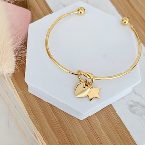 May include: A gold bangle bracelet with a knotted design and two charms: a heart and a star.
