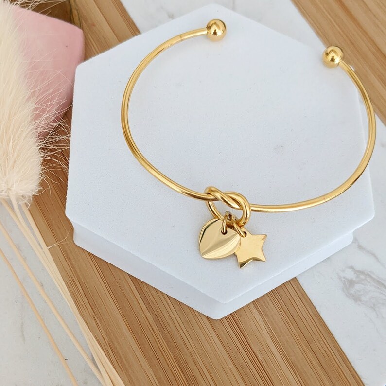 May include: A gold bangle bracelet with a knotted design and two charms: a heart and a star.