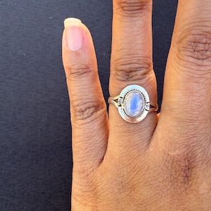 Può includere: Un anello d'argento con una grande pietra ovale blu chiaro. La pietra è incastonata in una lunetta d'argento con un bordo a forma di corda. L'anello è su una mano con uno sfondo scuro.