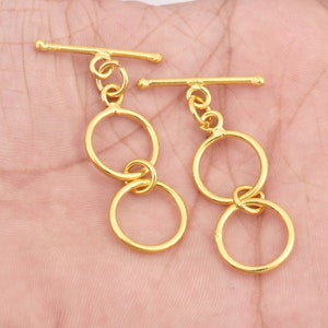 May include: Two gold-toned toggle clasps with double circle designs. Each clasp features two interlocking circles, one larger than the other.
